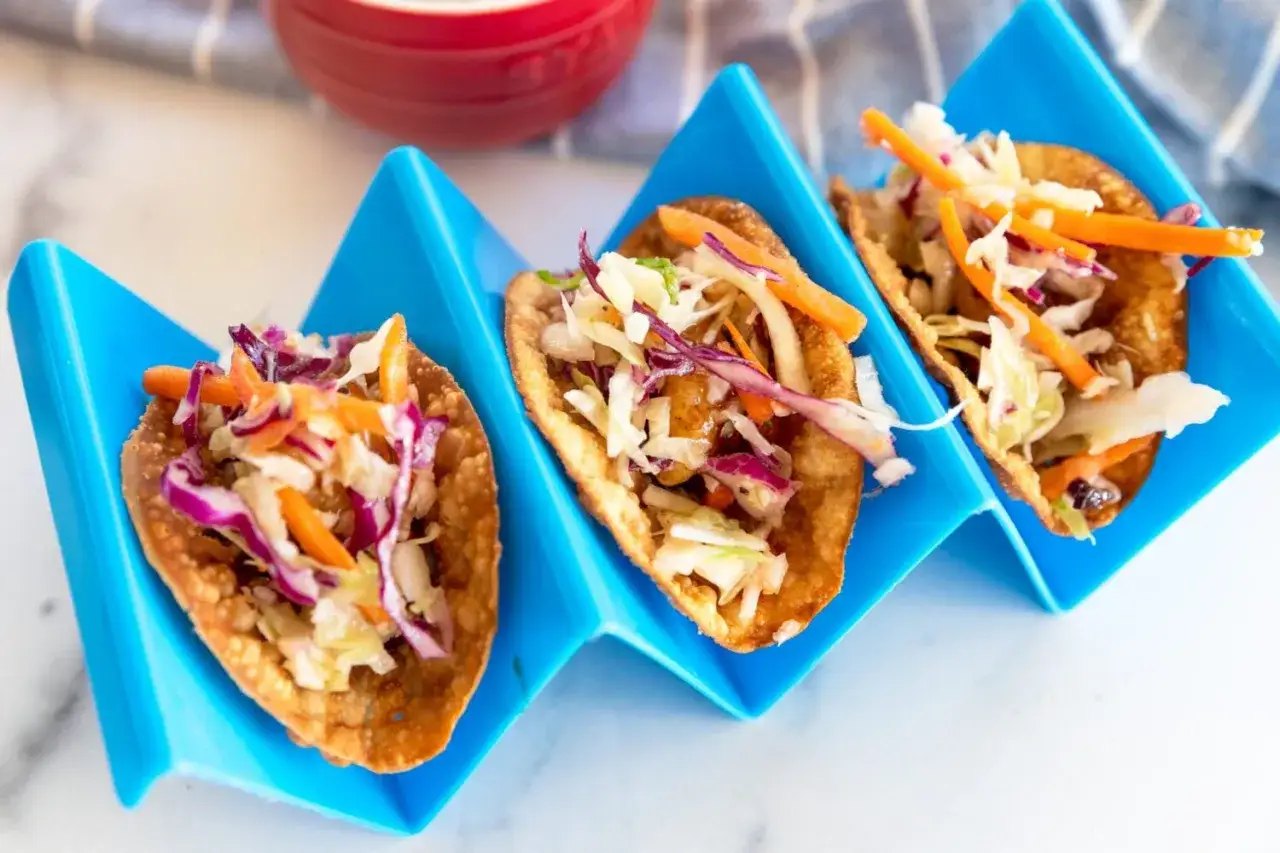 Tre l&auml;ckra asiatiska tacos med krispig topping av k&aring;l och mor&ouml;tter i bl&aring;a h&aring;llare.