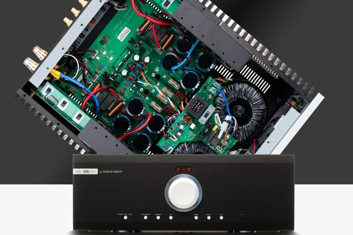Wnętrze wzmacniacza Musical Fidelity M6 500i z widocznymi kondensatorami i transformatorem. Z przodu czarna obudowa z pokrętłem i przyciskami.