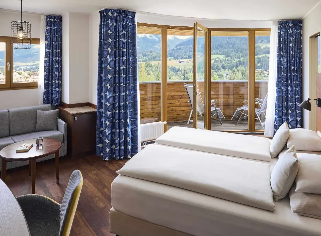 Gemütliches Zimmer im Robinson Fieberbrunn mit Bergblick, zwei Betten, Sofa und Balkon.