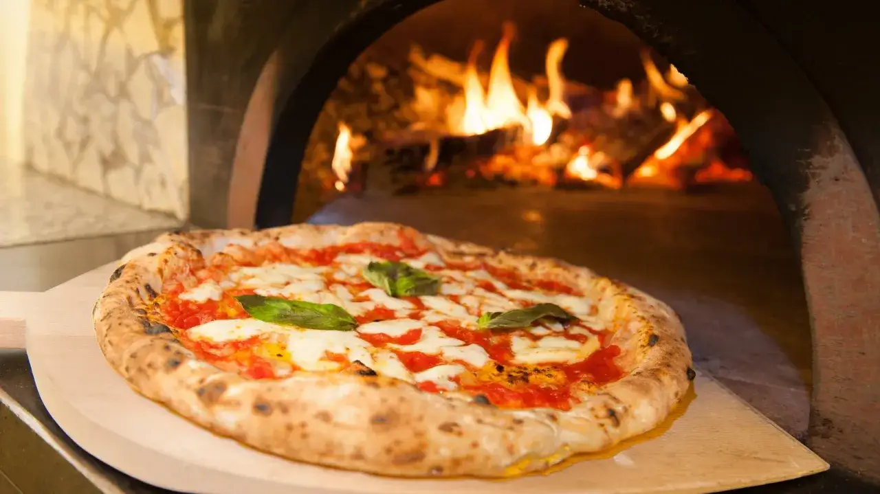Frisch gebackene Pizza Margherita auf einem Holzschieber, bereit für den Ofen. Das perfekte Pizza Margherita Rezept.