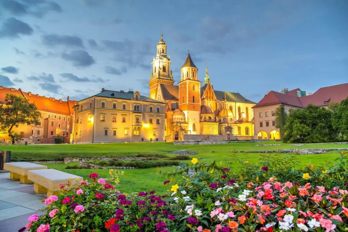 Kraków. Wawel, najstarszy kościół w Polsce, lśni w wieczornym świetle. Przed nim kwitnące kwiaty i zielony trawnik.