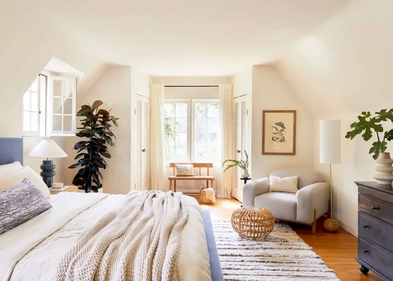Chambre lumineuse avec un plafond blanc, idéal pour agrandir la pièce. Un grand ficus, un fauteuil confortable et un lit douillet invitent à la détente.