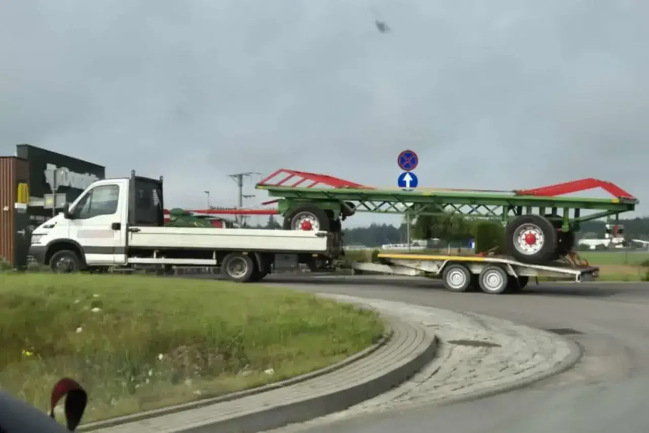 Transport przyczepy kempingowej na lawecie. Biała ciężarówka z platformą przewozi zieloną przyczepę z czerwonymi elementami.