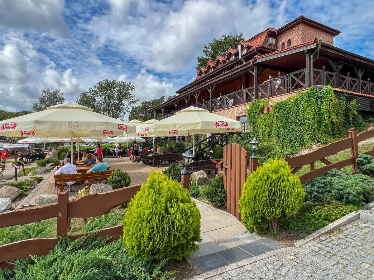 Letnia atmosfera w jednej z najlepszych restauracji na Mazurach. Goście relaksują się pod parasolami, ciesząc się widokiem na jezioro.