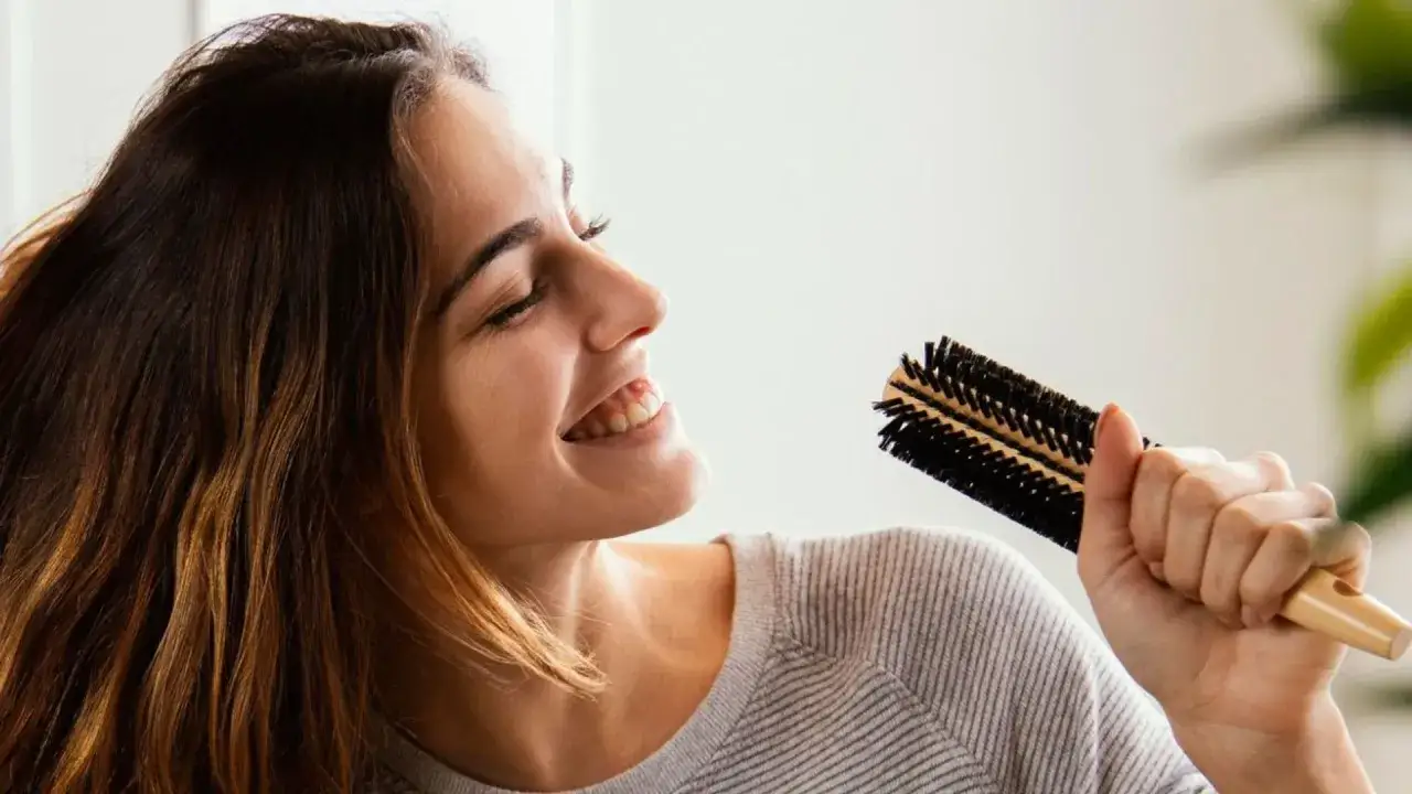 Mujer sonriente con cepillo, aprendiendo como alisar el pelo sin plancha.