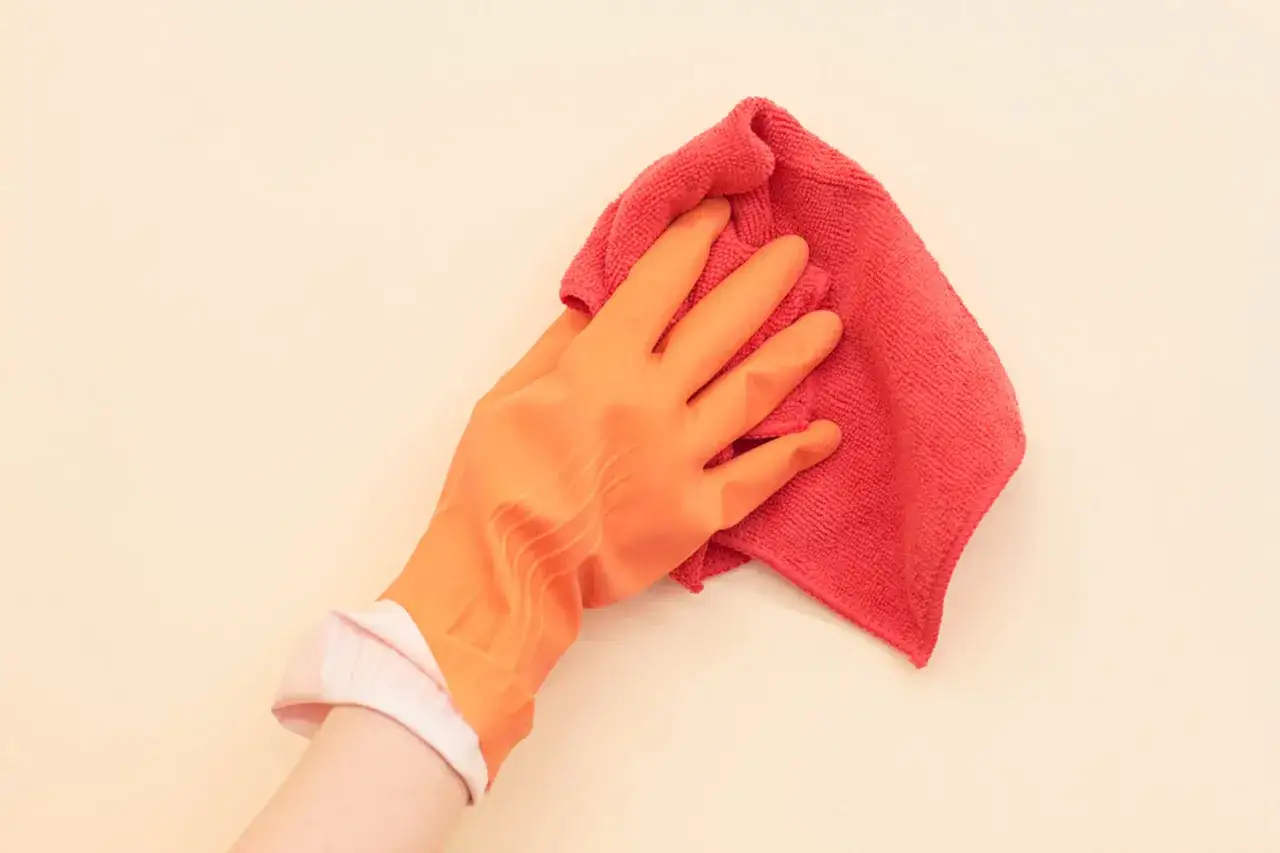 Mano con guante naranja limpiando una pared con un paño rojo. Guía rápida sobre como limpiar paredes.