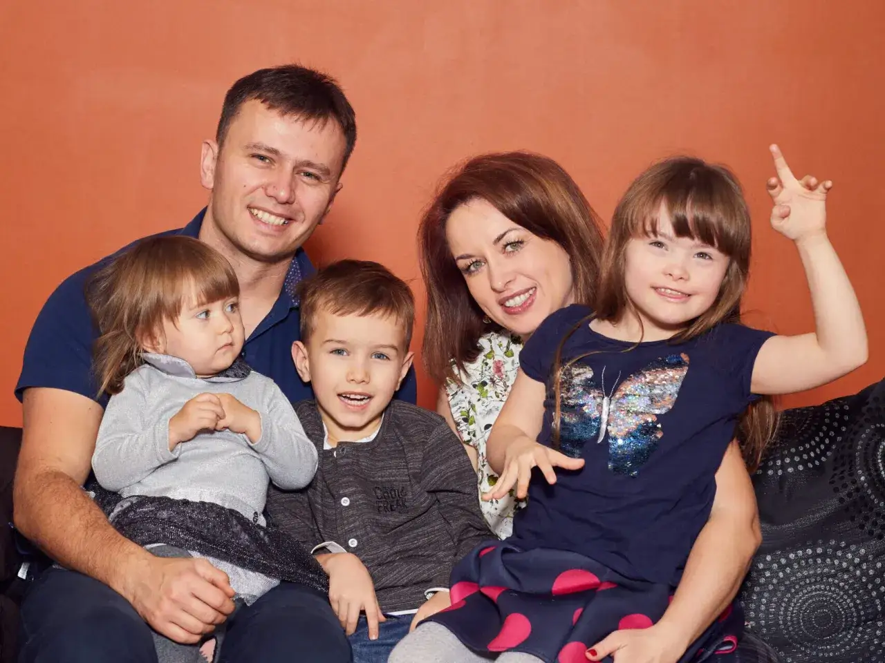 Szczęśliwa rodzina z dziećmi, w tym dziewczynką z zespołem Downa, pozuje do zdjęcia.