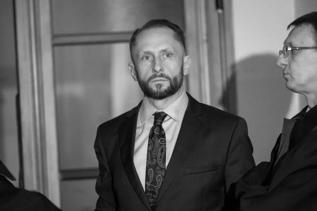 Kamil Durczok w garniturze, z charakterystyczną brodą, w kadrze z innym mężczyzną. Prawdopodobnie podczas nagrania 