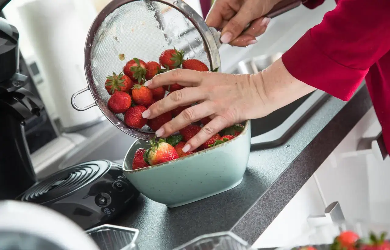 Hände waschen Erdbeeren in einer Schüssel. Frische rote Früchte werden aus einem Sieb in eine hellblaue Schale gegeben.