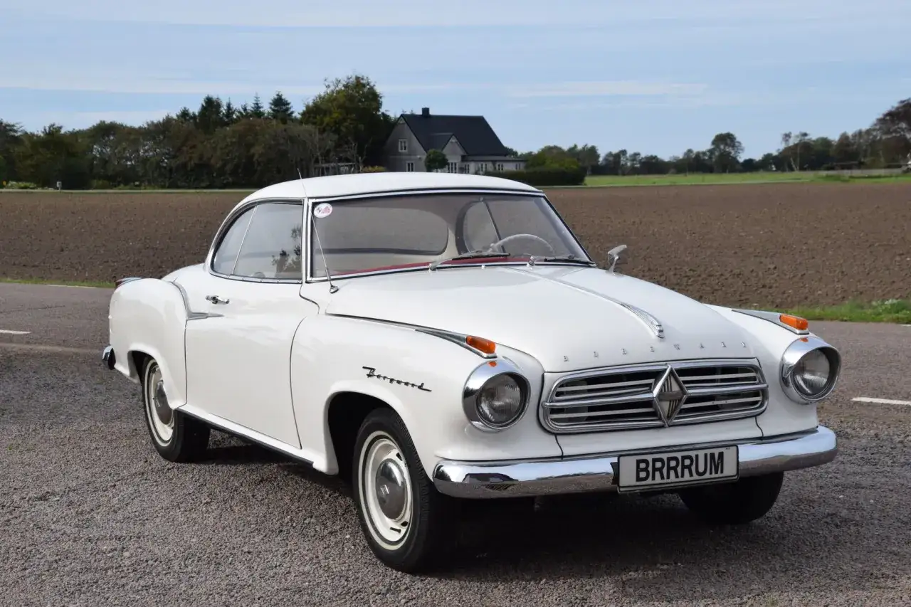 Vit Borgward Isabella står parkerad på grusväg. Bilen har en klassisk design med kromdetaljer och en röd interiör.
