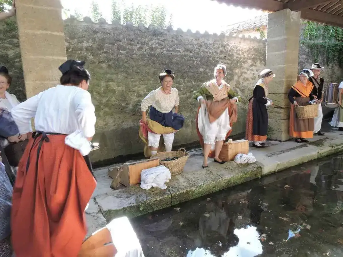 Des femmes en costumes d'&eacute;poque s'adonnent &agrave; la t&acirc;che de laver le linge autrefois, pr&egrave;s d'un lavoir.
