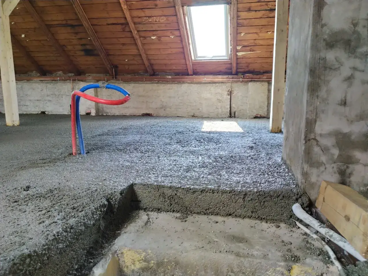 Świeżo wylany **termo**beton na poddaszu, z widocznymi rurkami instalacji wodnej.
