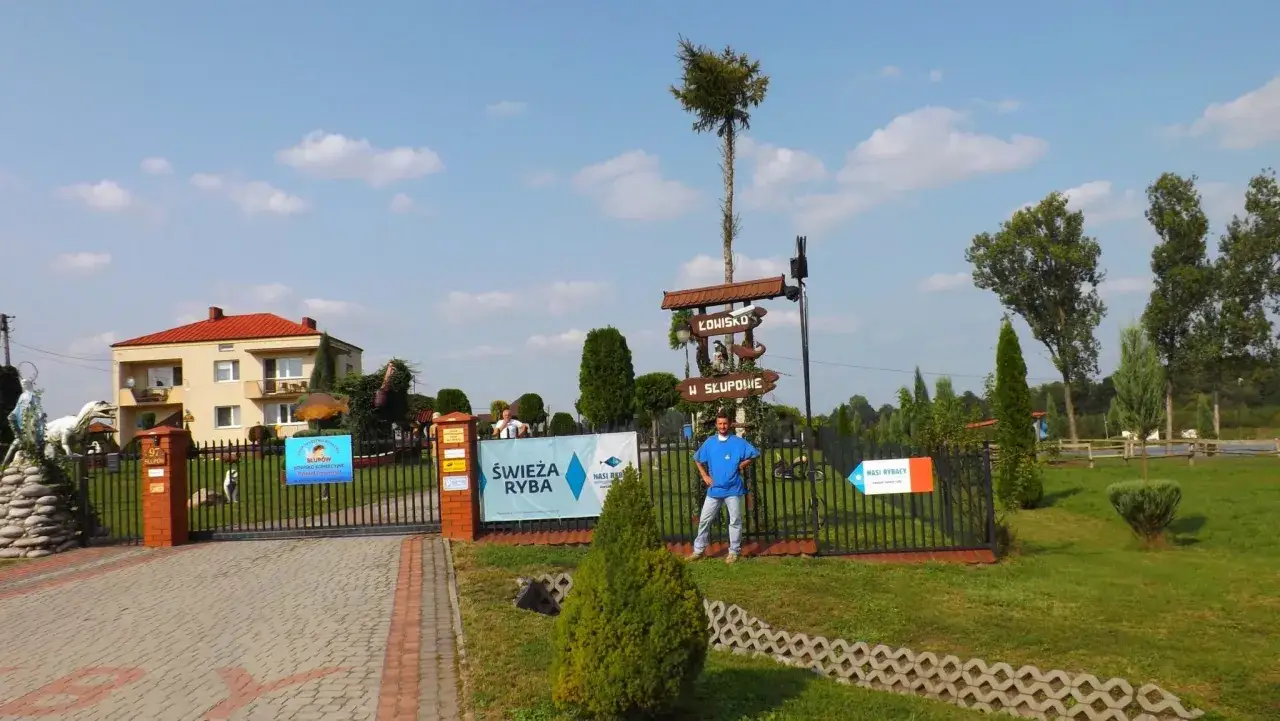Łowisko komercyjne w Słupowie. Wjazd na teren, tablice informacyjne i pracownik w niebieskiej koszulce.