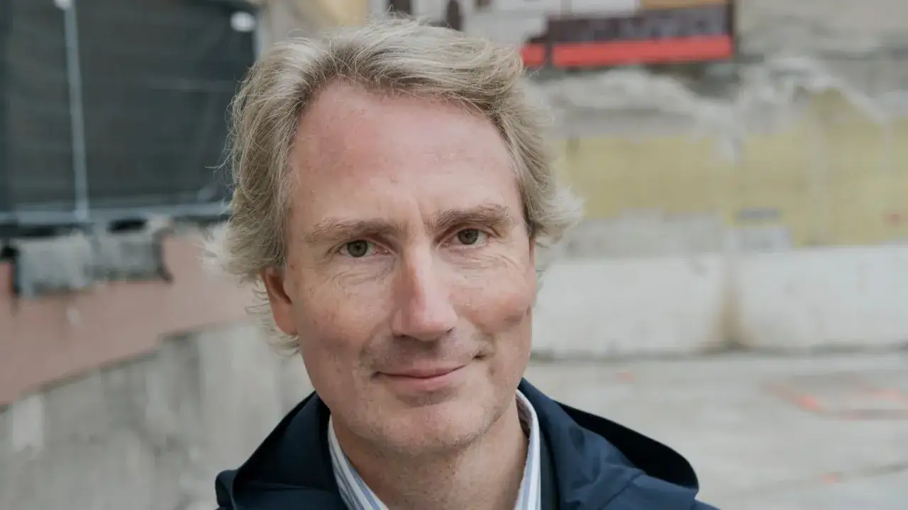 Erik Selin, en man med grått hår och en vänlig blick, står framför en byggarbetsplats.