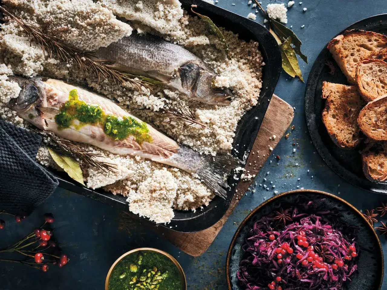 Zwei Wolfsbarsch-Fische in Salzkruste, verfeinert mit Kräutern und Beilagen wie Brot und Rotkohl.