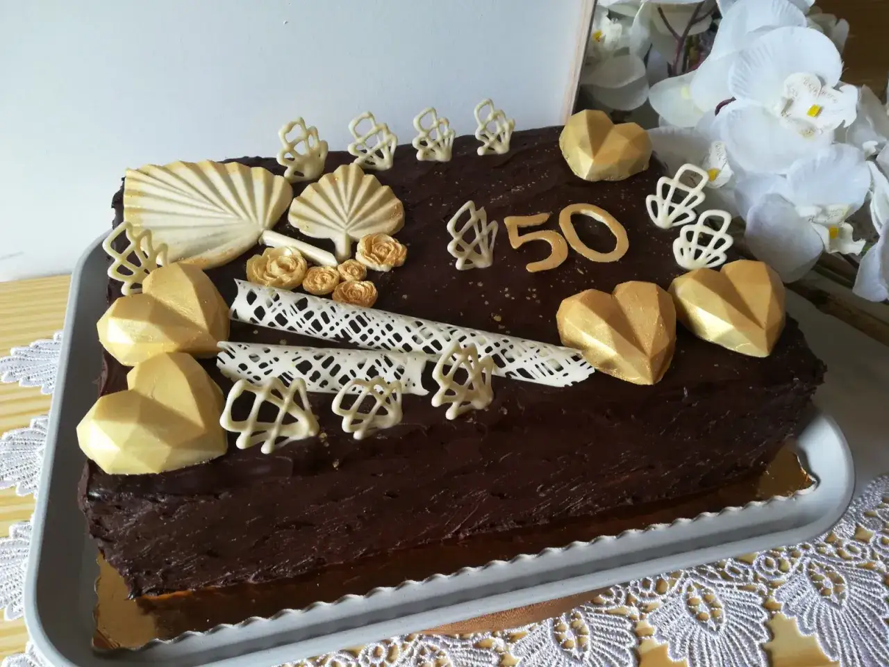 Elegancki tort prostokątny na 50. urodziny. Złote serca, wachlarze i kwiaty z czekolady pokazują, jak udekorować tort prostokątny.