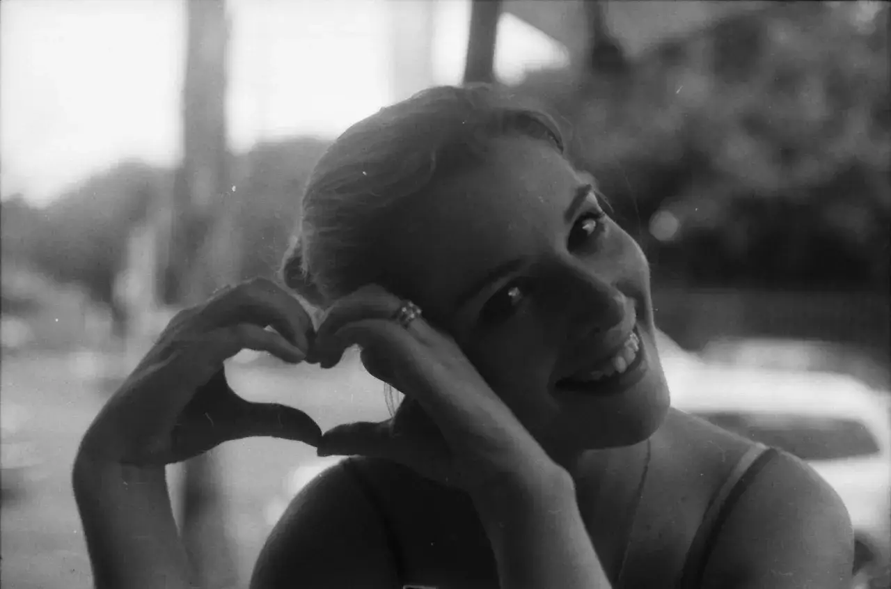 A woman smiles, forming a heart with her hands. Captured on Ilford FP4+, the image has a timeless, classic feel.