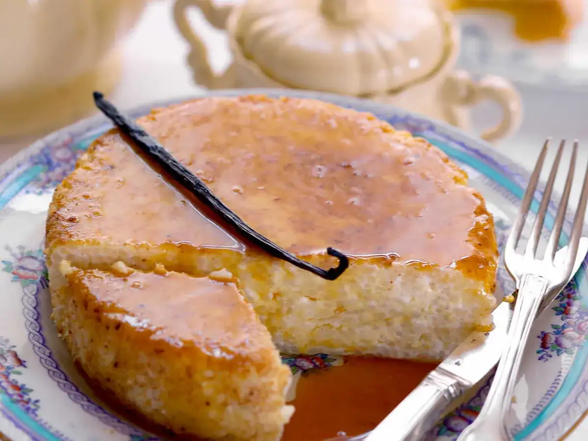 Un d&eacute;licieux g&acirc;teau de riz cr&eacute;meux, napp&eacute; de caramel et garni d'une gousse de vanille, servi sur une assiette orn&eacute;e.