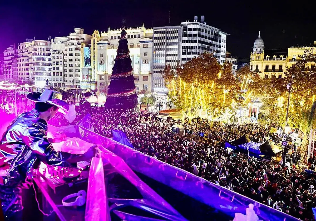 DJ anima la nit de cap d'any a una plaça plena de gent, amb un arbre de Nadal gegant i llums festives.