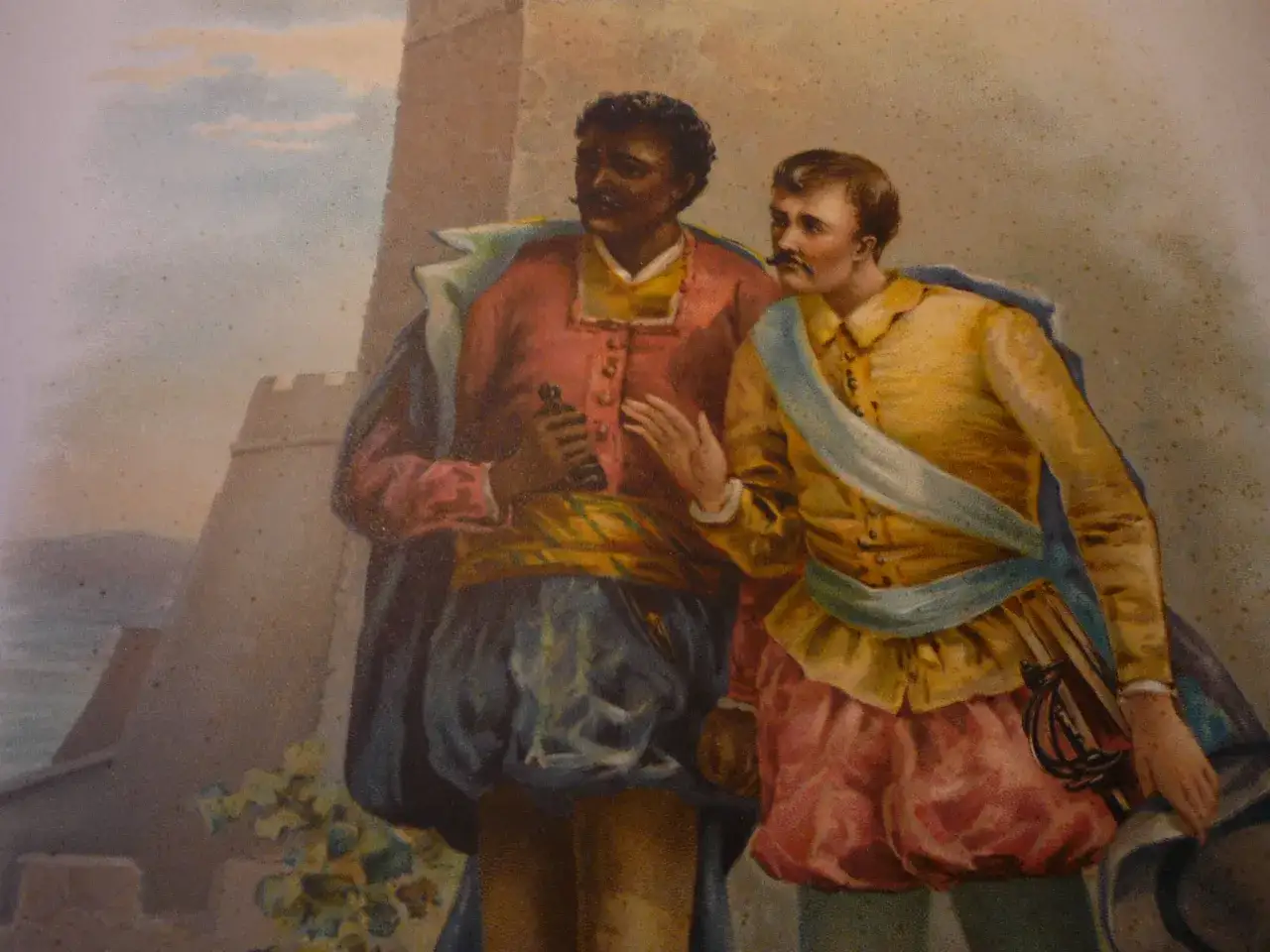 Dwóch mężczyzn w strojach z epoki, jeden ciemnoskóry, drugi jasnoskóry, rozmawia przy zamku. Otello kim był? Bohaterem tragedii Szekspira.