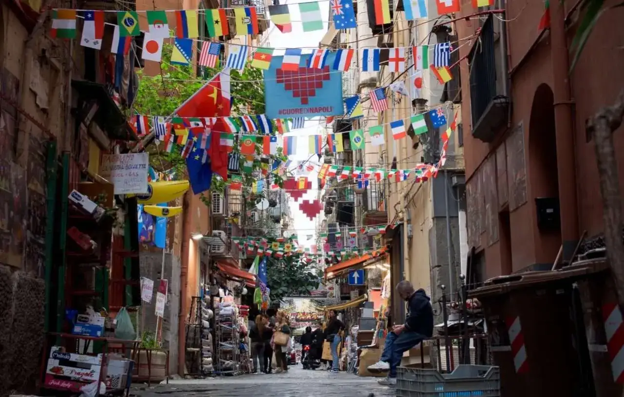Un vicolo napoletano pieno di bandiere da tutto il mondo, cuori rossi e **esclamazioni in napoletano** sui cartelli. Che meraviglia!