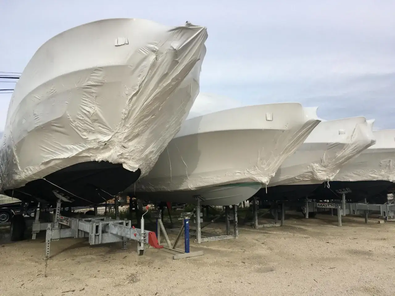 Plusieurs bateaux sont bâchés pour leur hivernage, prêts à affronter la saison froide sur des remorques et des supports.