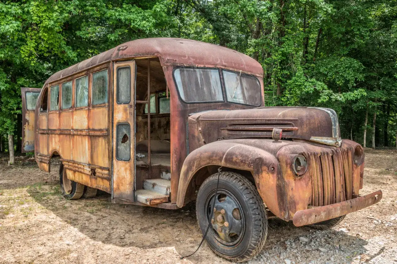 Rdza, zniszczony autobus szkolny na tle lasu. Skutki wyboru nietypowej lokalizacji (industrial, szklarnia) dla logistyki gości.