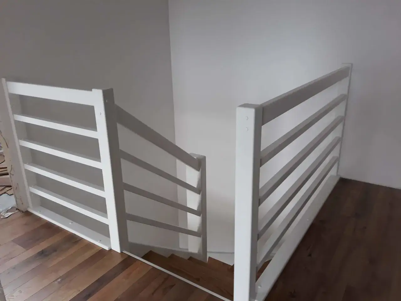 Białe, nowoczesne schody angielskie z drewnianymi stopniami i podłogą. Proste balustrady z poziomymi szczebelkami.