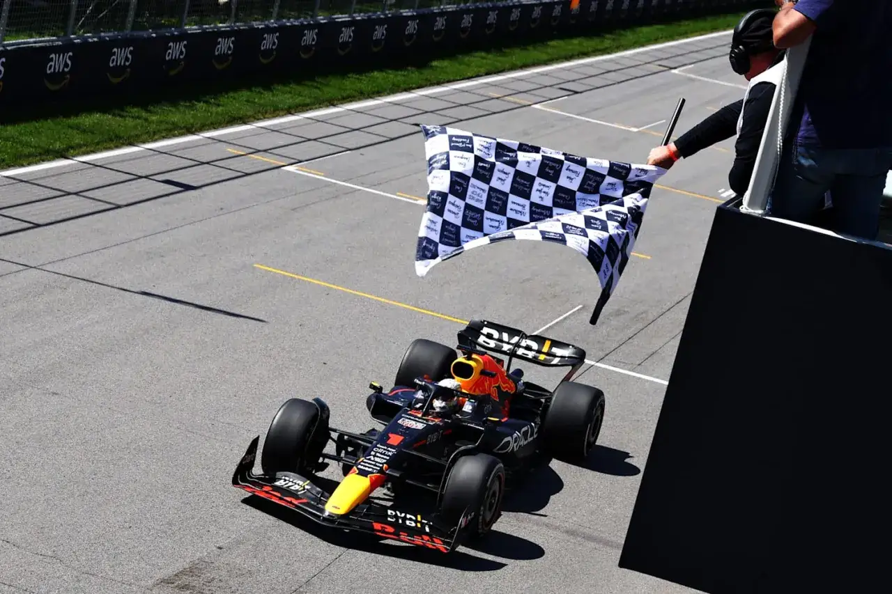 Kierowca bolidu Formuły 1 mija linię mety, machając szachownicą. To symboliczne zakończenie wyścigu, zgodne z zasadami Formuły 1.