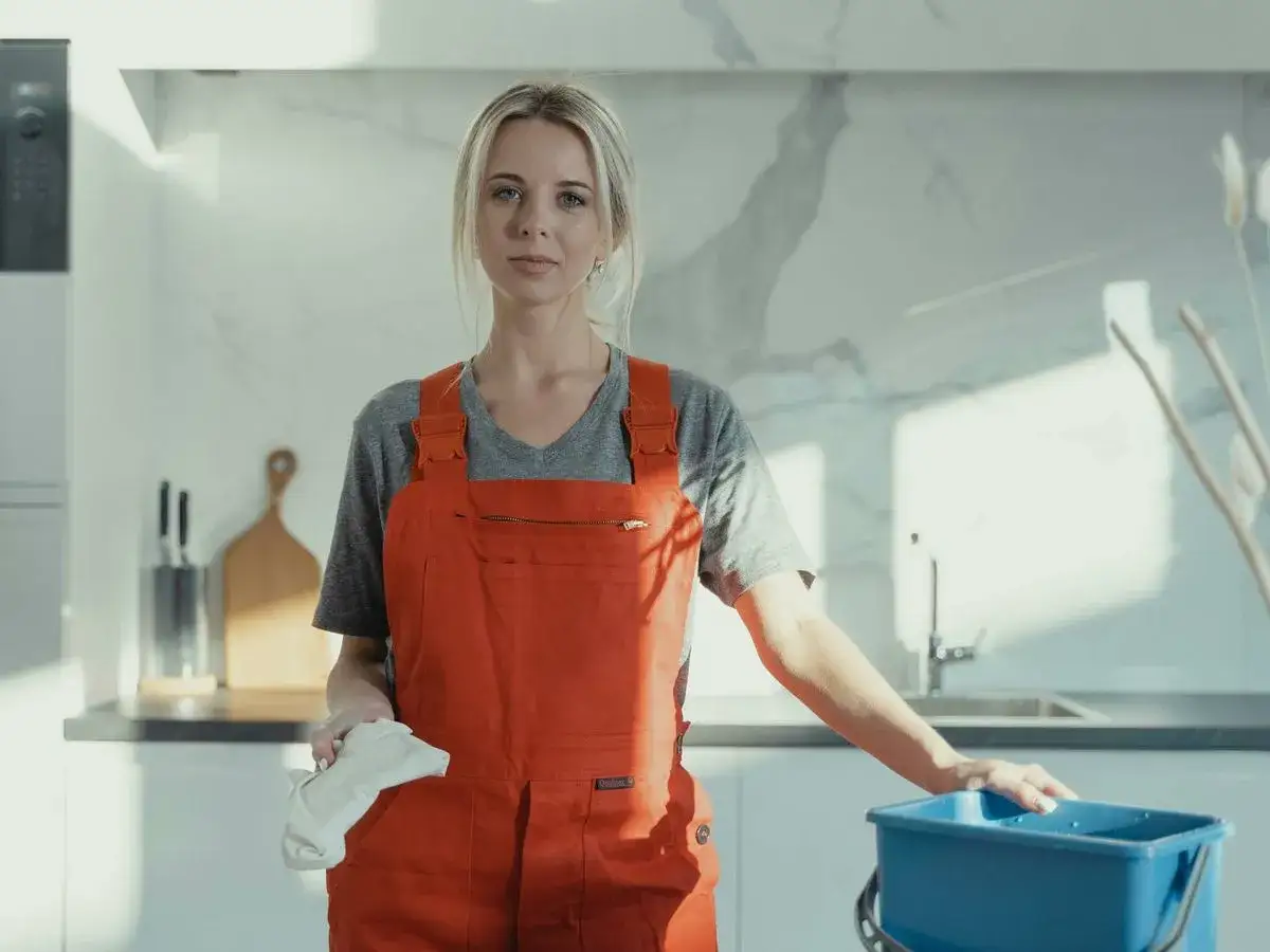 Mujer con mono naranja y trapo blanco, lista para aplicar trucos de limpieza en la cocina.
