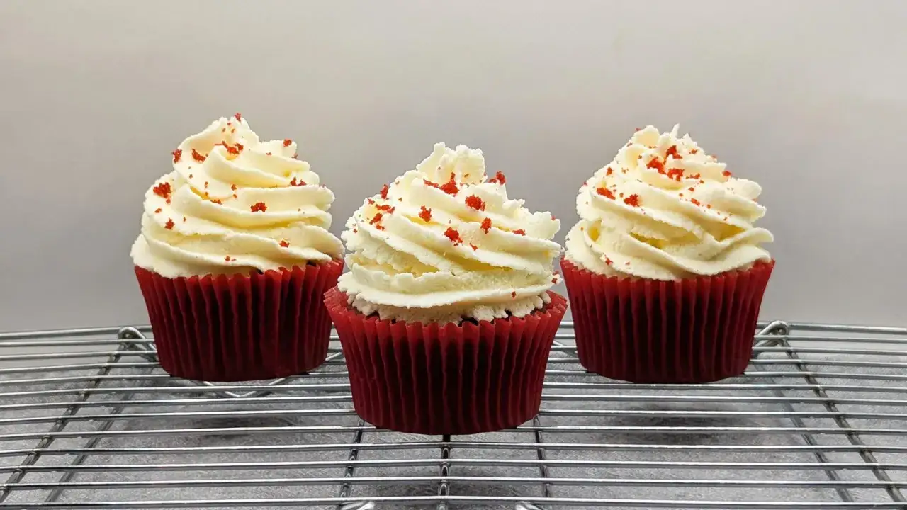 Drei rote Samtmuffins mit wei&szlig;er Creme und roten Streuseln, perfekt f&uuml;r ein Red Velvet Muffins Rezept.