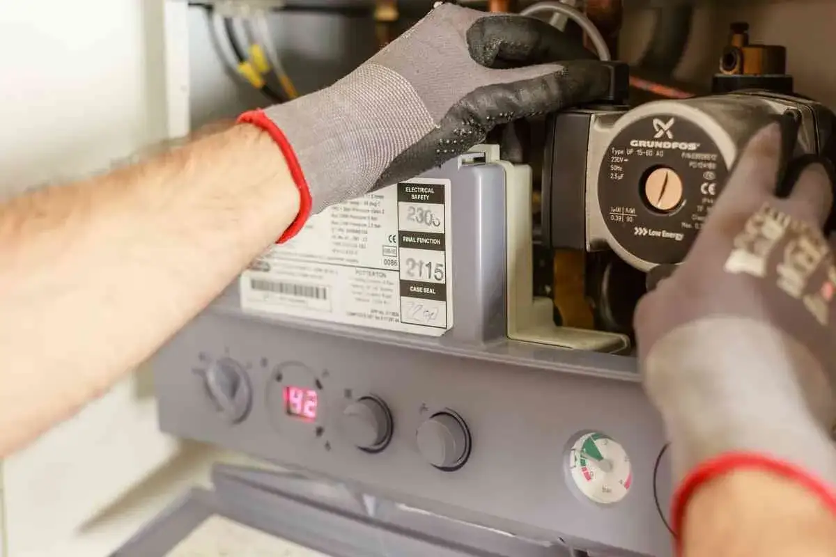 Main d'un technicien ajustant une chaudi&egrave;re Frisquet. Avis sur la fiabilit&eacute; et l'entretien de cet appareil de chauffage.