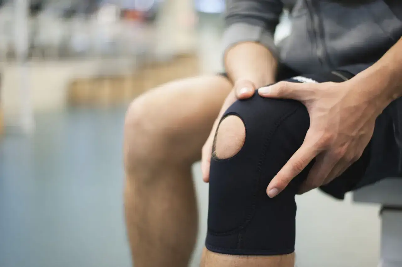 Mann hält schmerzendes Knie mit schwarzer Kniebandage. Die Kniebandage verursacht Schmerzen, die er nicht ignorieren kann.