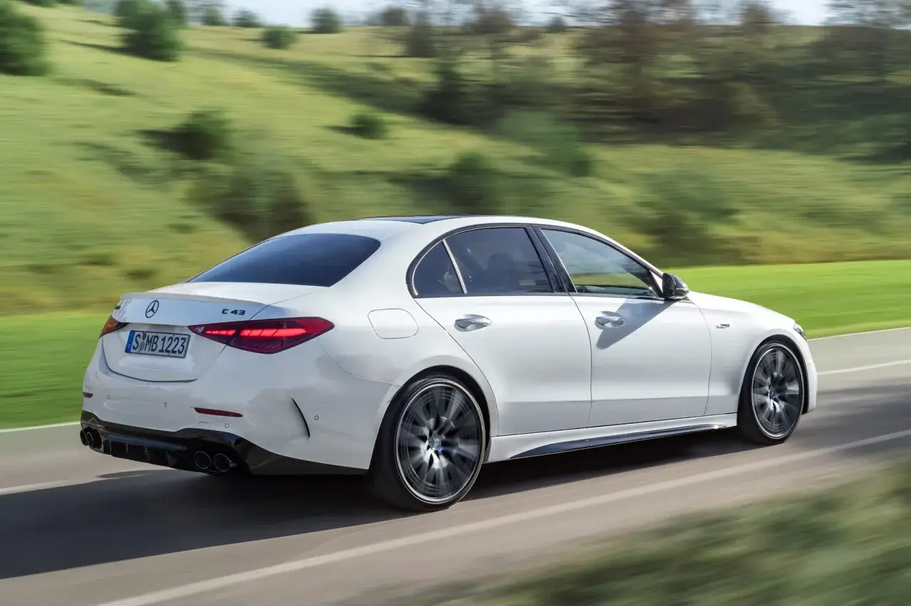 Biały Mercedes C43 AMG pędzi po drodze, otoczony zielonymi wzgórzami.