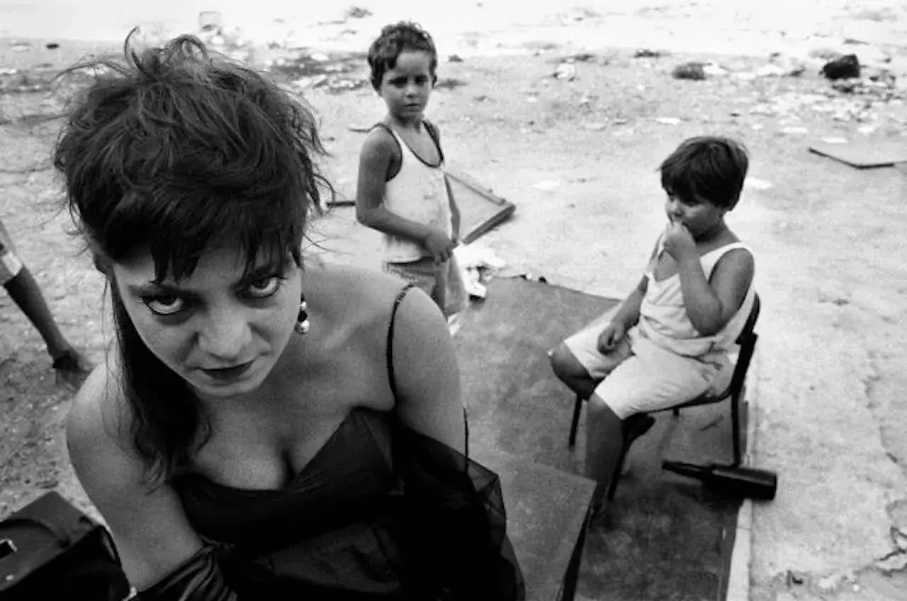 La fotografa famosa italiana cattura uno sguardo intenso, con due bambini sullo sfondo in un ambiente desolato.