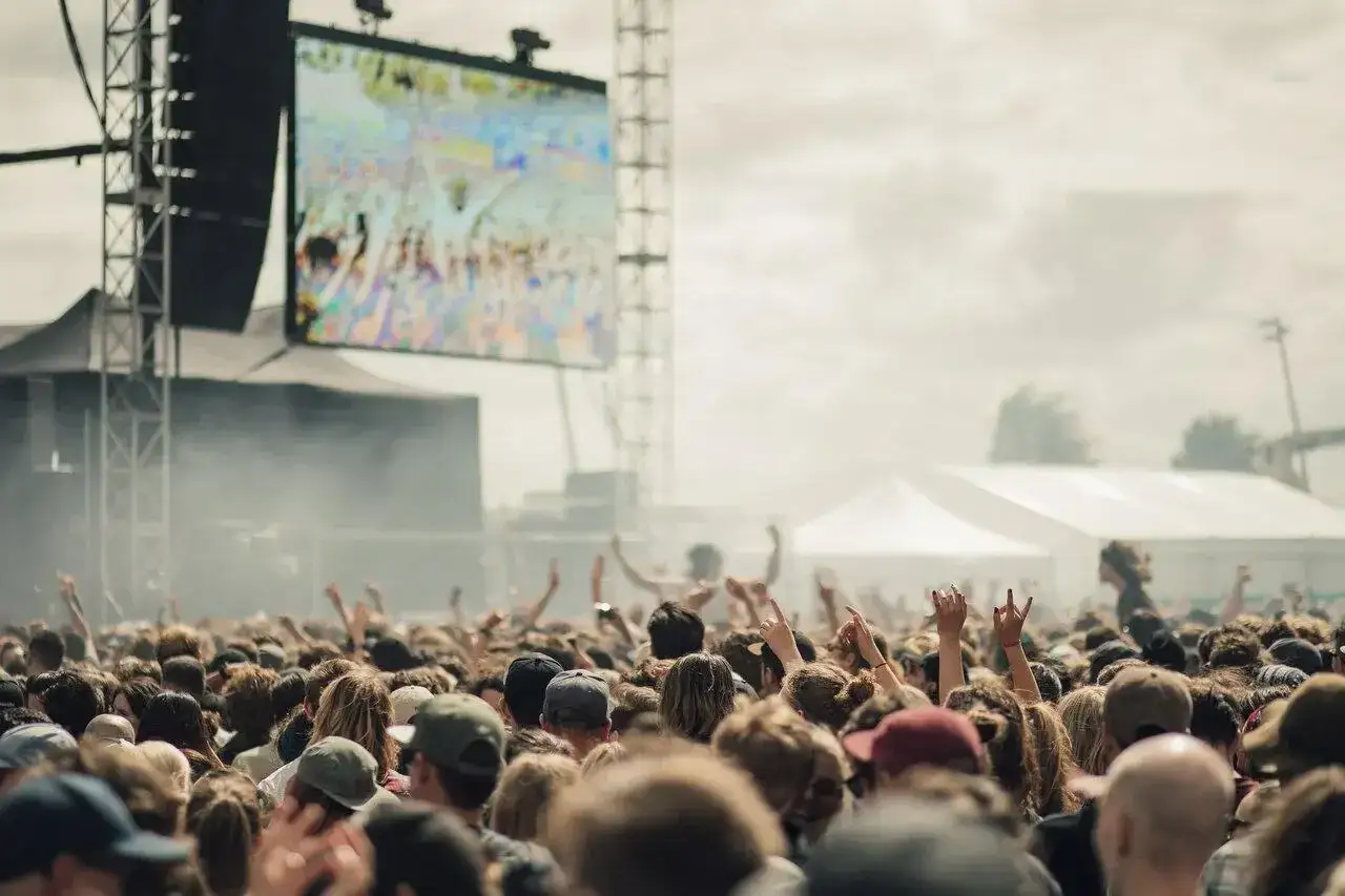 Tłum ludzi na Jarocin Festiwal, ręce w górze, wielki ekran z koncertem w tle.