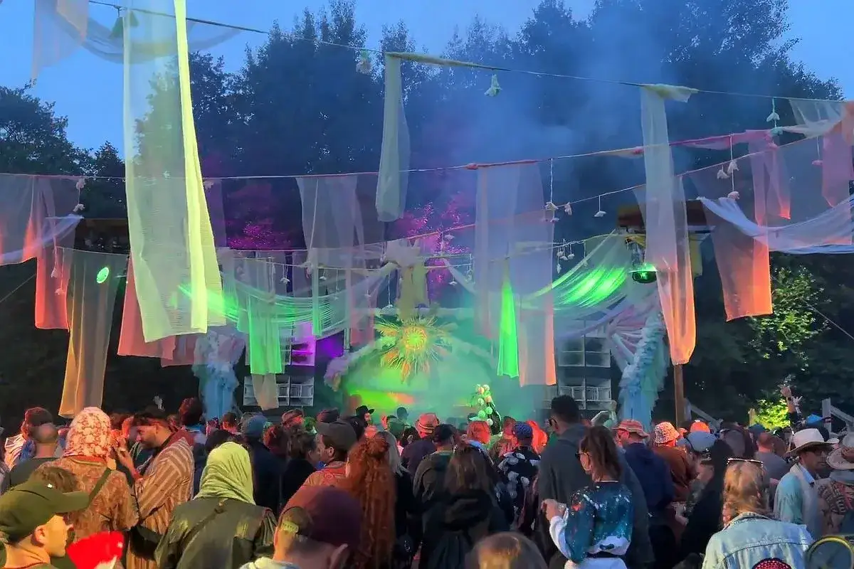 Tłumy ludzi na letnim festiwalu, kolorowe tkaniny i światła tworzą magiczną atmosferę.