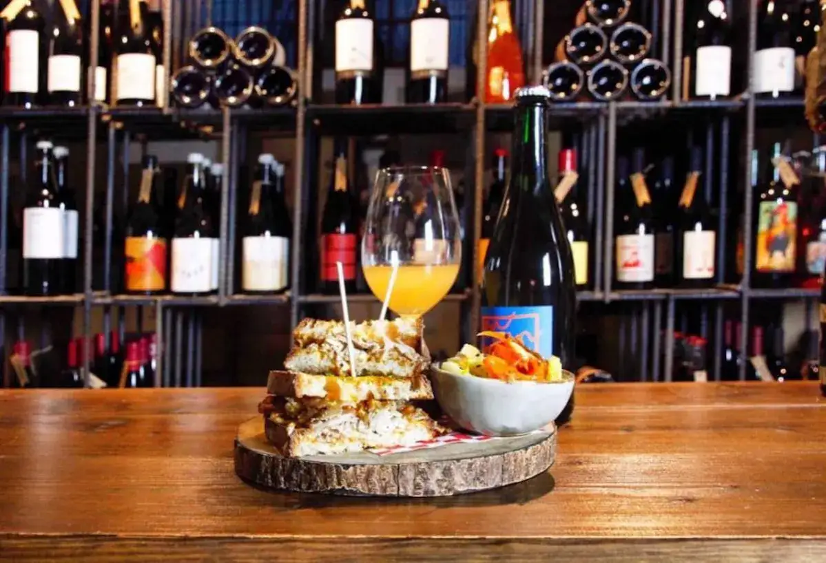 Un delicioso s&aacute;ndwich apilado, una copa de vino y una ensalada colorida en la barra de un restaurante de vinos.
