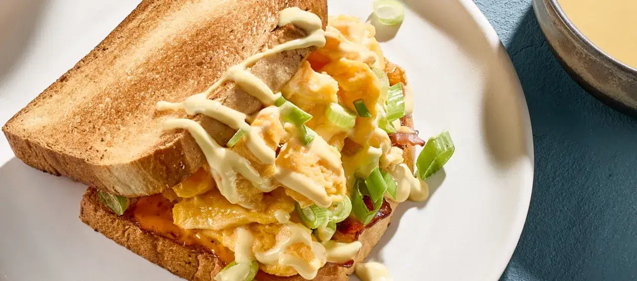 Ein herzhaftes Eggdrop Sandwich mit R&uuml;hrei, Fr&uuml;hlingszwiebeln und einer cremigen Sauce auf ger&ouml;stetem Brot.