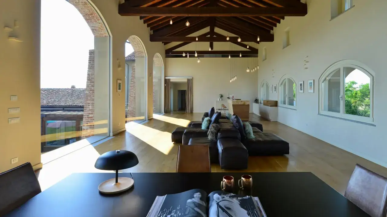 Geräumige Loggia mit Ledersofa, Holzbalken und großen Fenstern, die viel Licht hereinlassen.