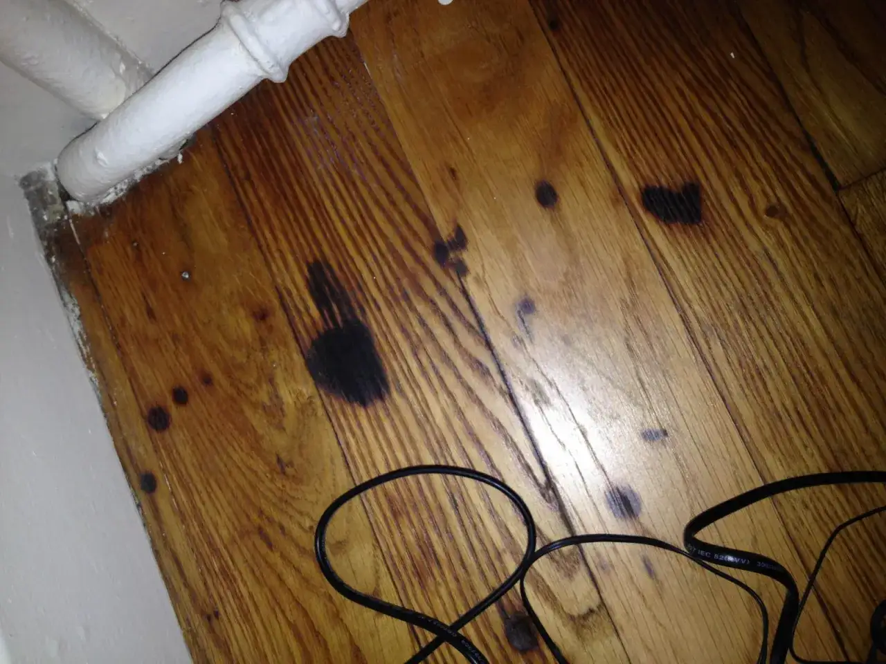 Parquet vitrifié avec des traces sombres, peut-être des marques de frottement à enlever. Des câbles noirs sont posés au sol.