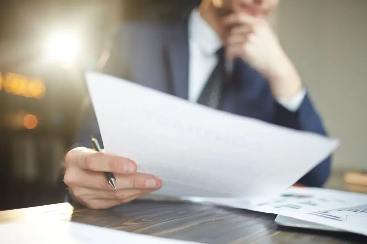 Mężczyzna w garniturze analizuje dokumenty, zastanawiając się, co dalej, gdy firma ogłasza upadłość, a pracownicy szukają odpowiedzi.