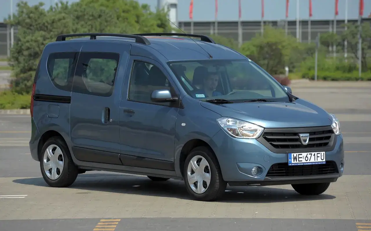 Niebieski Dacia Lodgy, praktyczny mpv za niskie, z relingami dachowymi i przyciemnianymi szybami, stoi na parkingu.