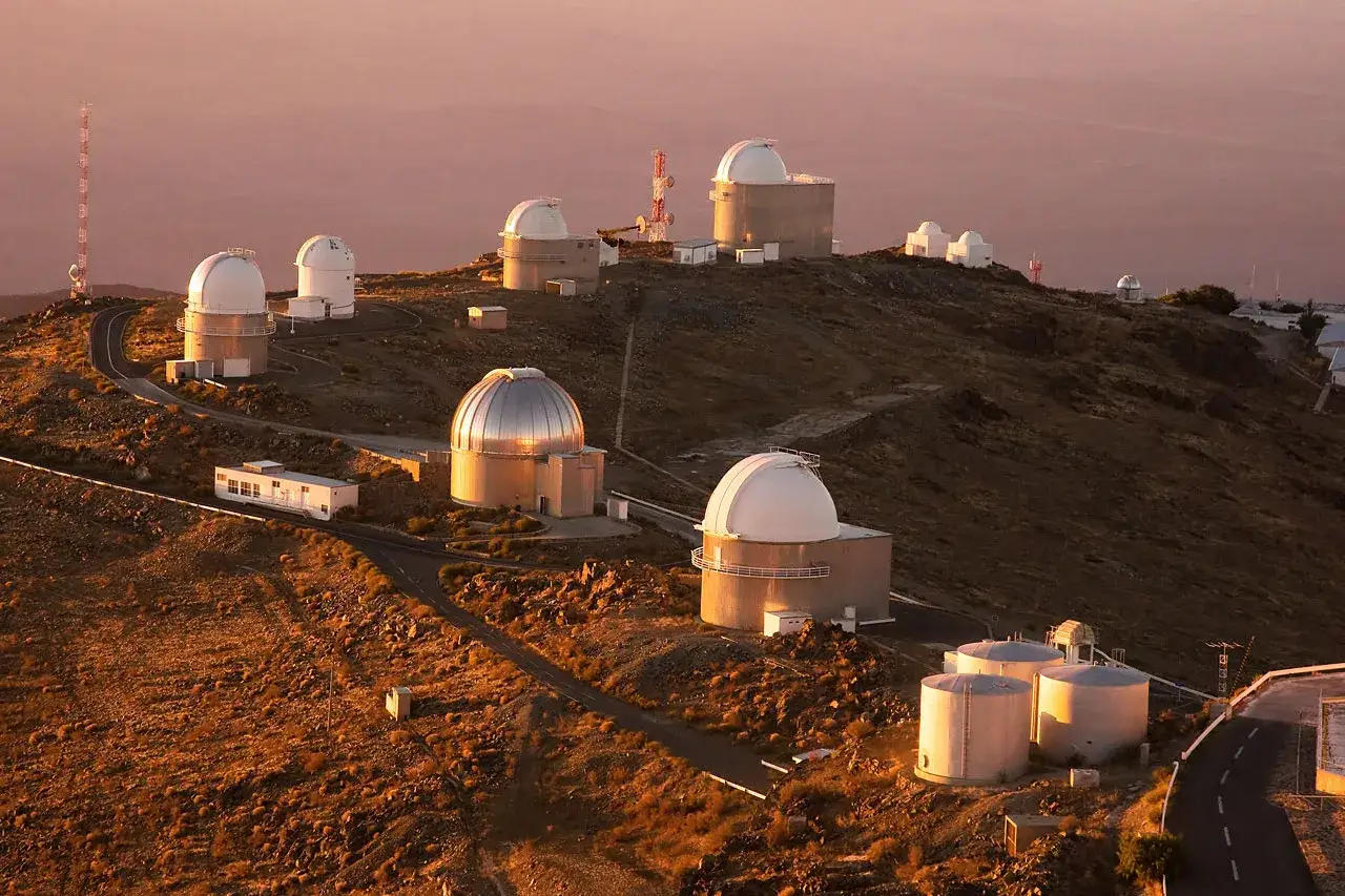 Obserwatoria astronomiczne na wzgórzu La Silla, oświetlone złotym blaskiem zachodzącego słońca.