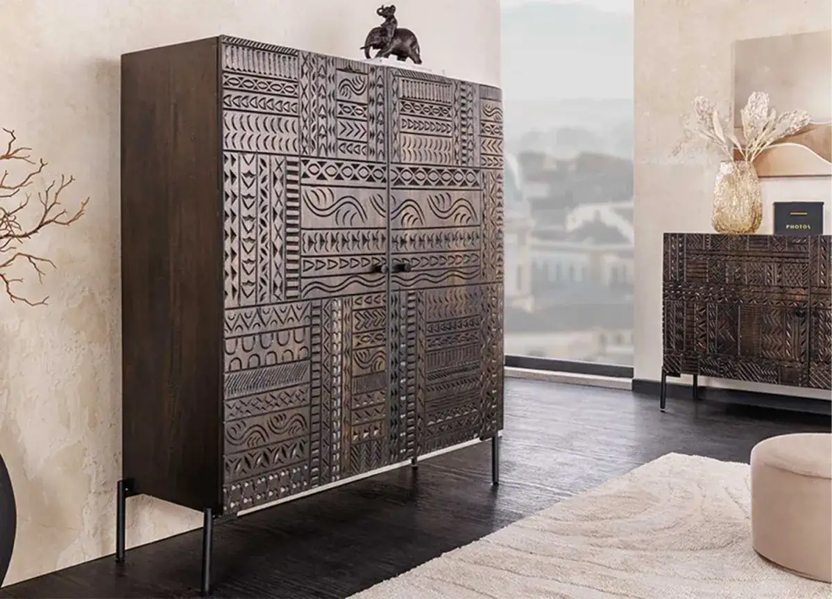 Buffet en bois sombre aux motifs ethniques sculptés, avec une figurine d'éléphant sur le dessus. Sa hauteur est idéale pour un salon.