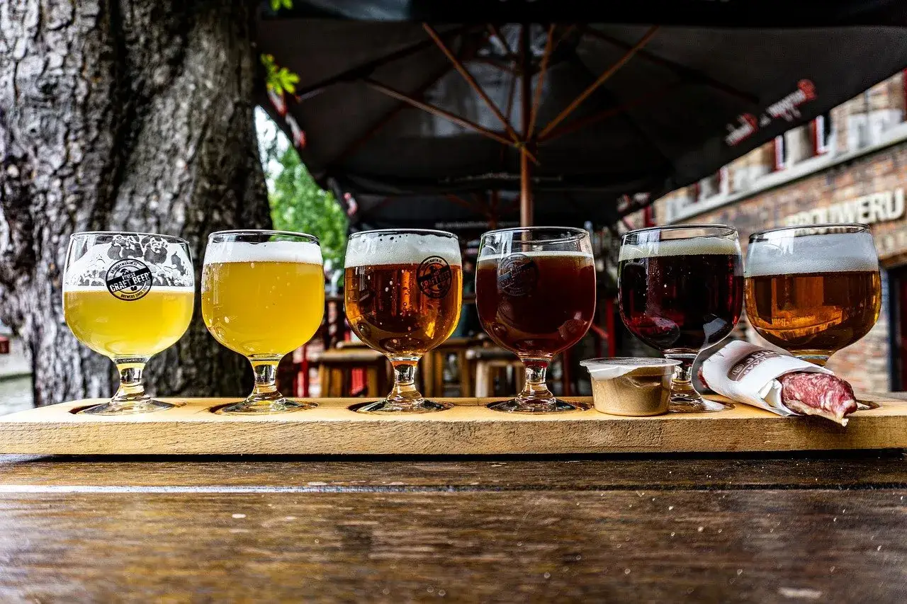 Degustacja piw: jasne, bursztynowe i ciemne piwo belgijskie. Obok kieliszków z piwem znajduje się sos i kawałek kiełbasy.