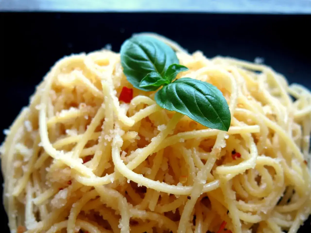 Makaron spaghetti z bułką tartą, czosnkiem i chili, ozdobiony listkiem bazylii. Pyszne danie, kt&oacute;re można przygotować z bułki tartej.