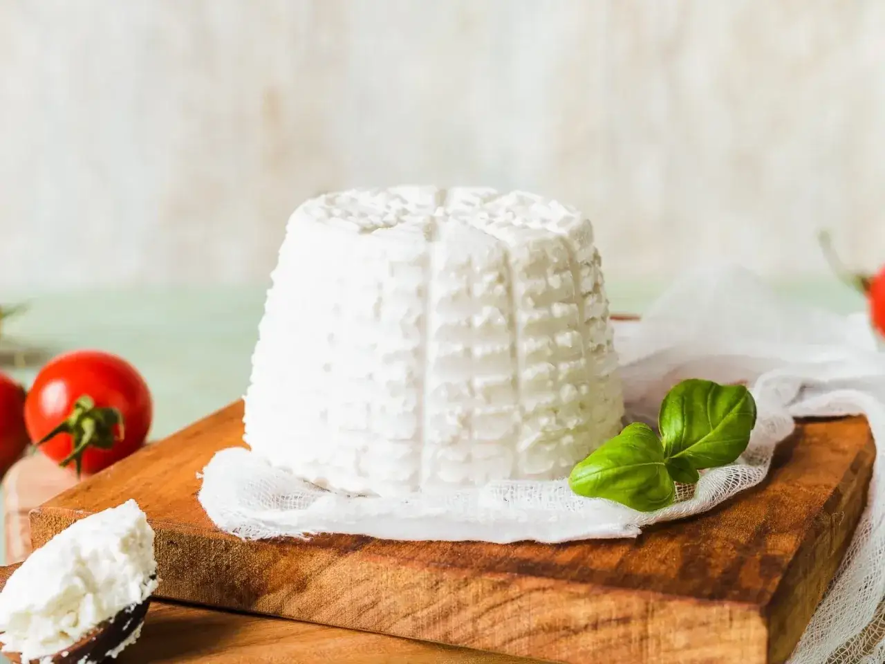 Świeża ricotta na desce, obok pomidorki i bazylia. Idealny ricotta skład na lekki posiłek.