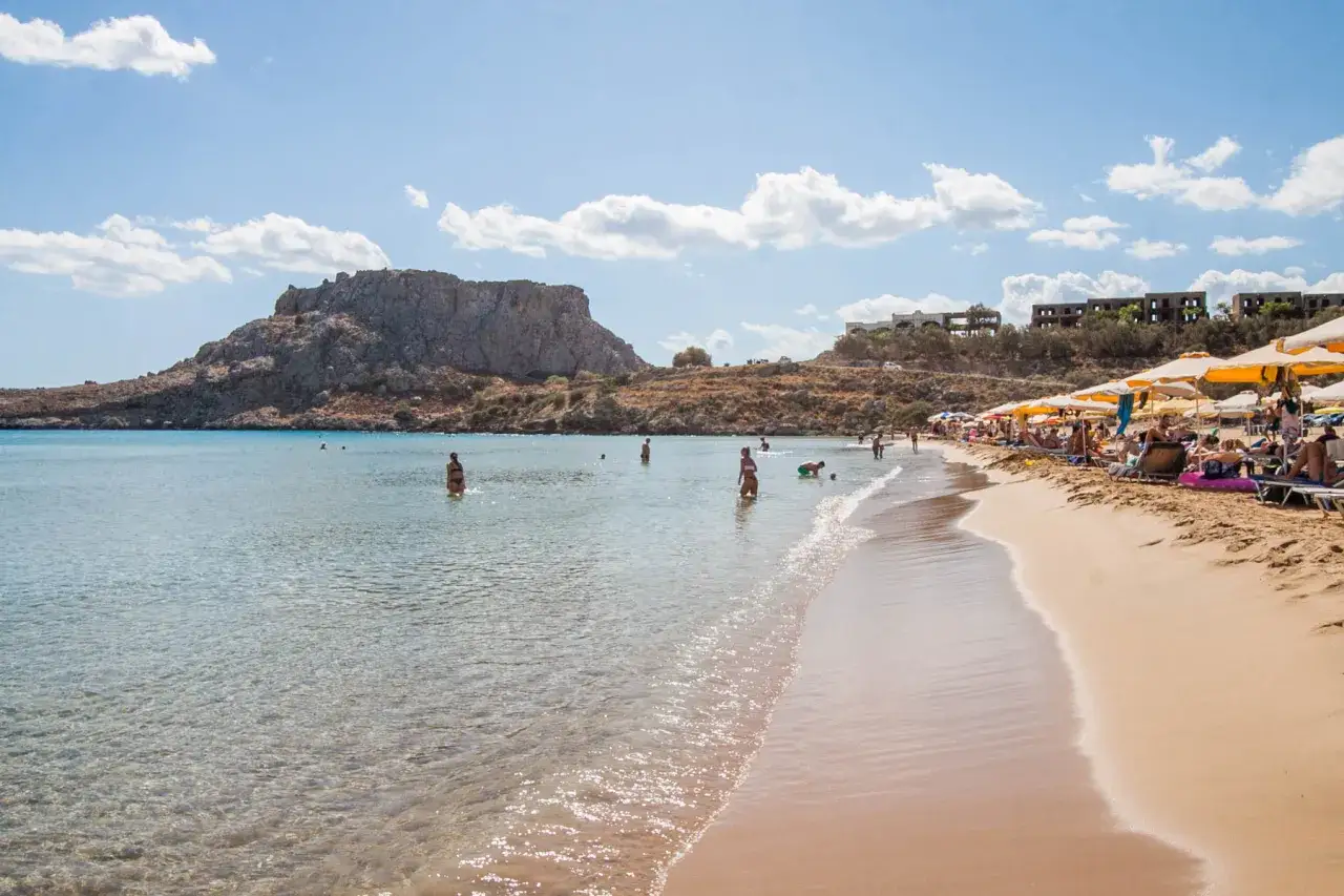 Piękna, słoneczna pogoda na Rodos w maju. Ludzie kąpią się w krystalicznie czystej wodzie, odpoczywają na plaży pod parasolami.