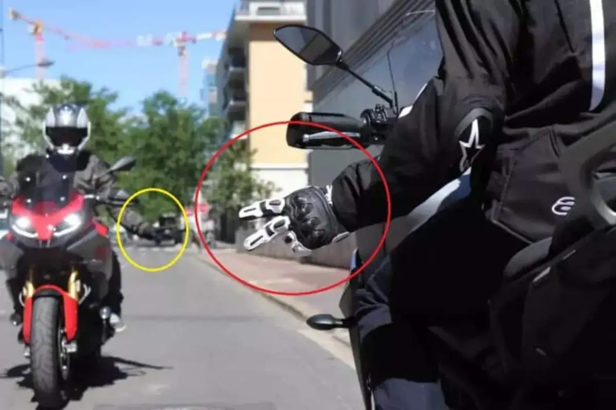 Mano guantata che fa il segno di pace, un gesto del linguaggio motociclisti. Un'altra moto in lontananza.